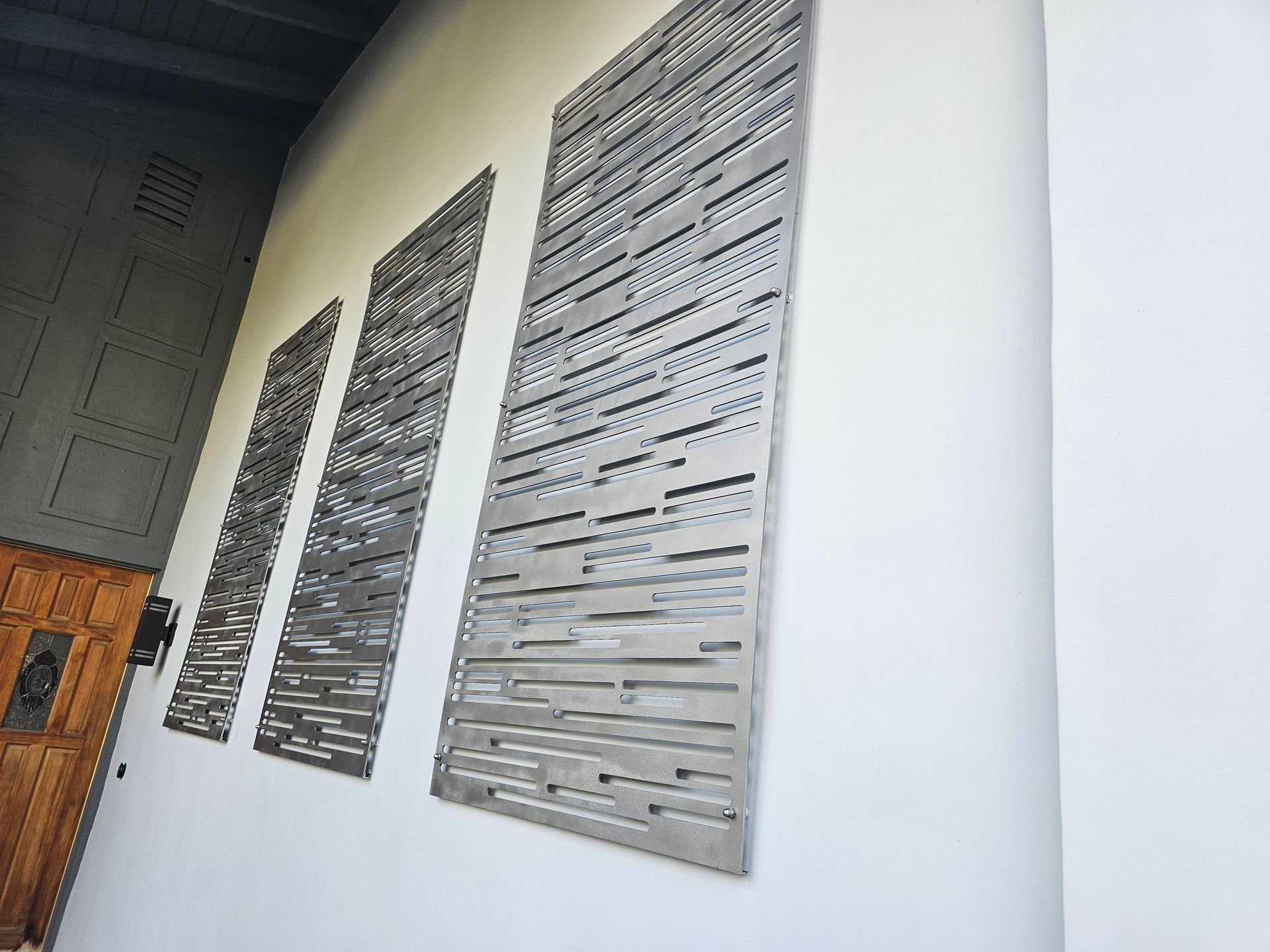 Three pieces of metal are hanging on a white wall.