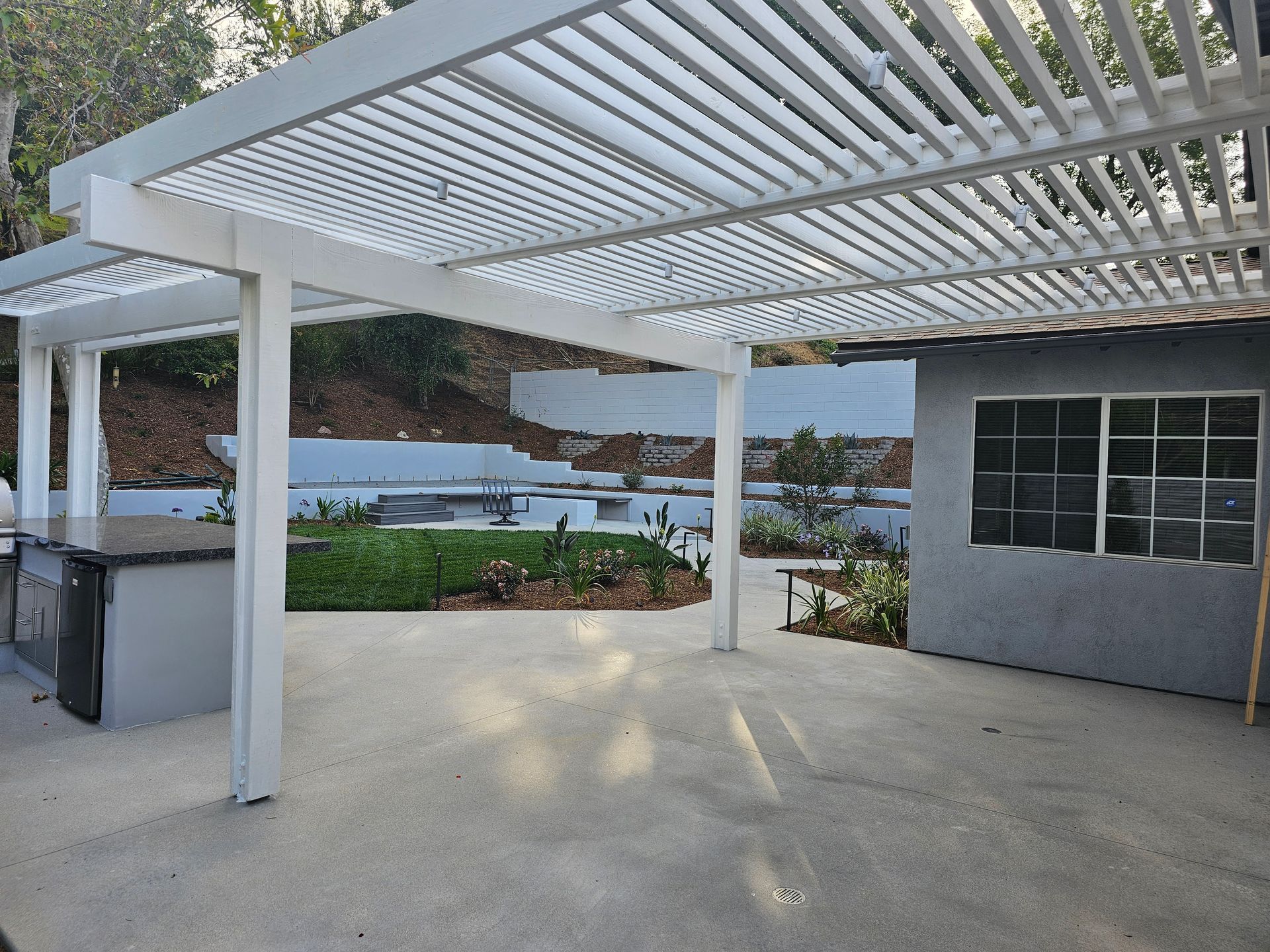 A white pergola is sitting on top of a concrete patio.