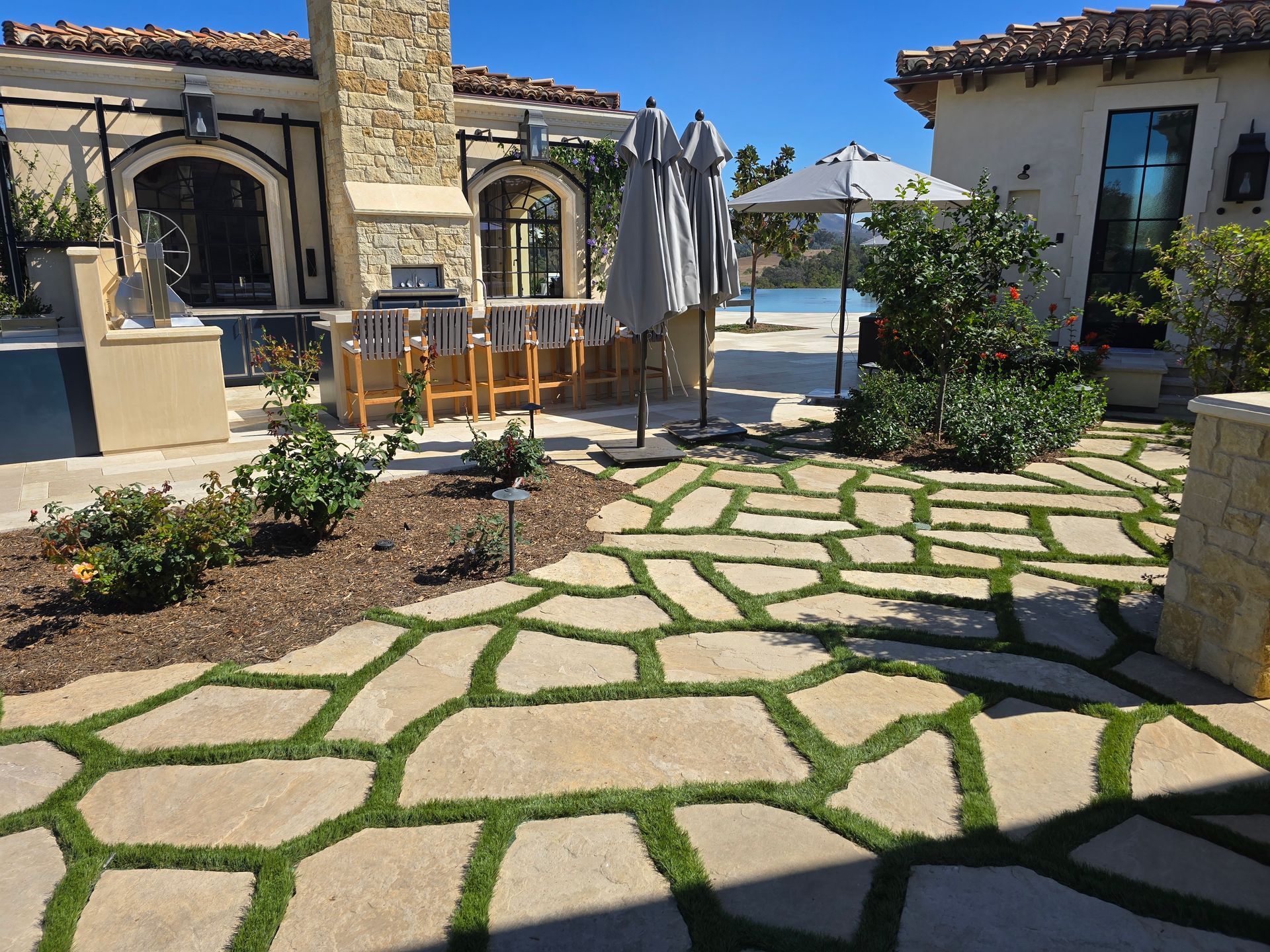 A stone walkway leading to a house with umbrellas and chairs.