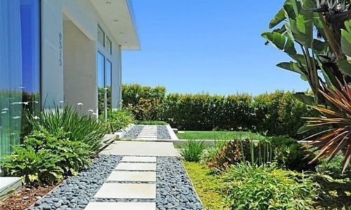 A walkway leading to a house surrounded by plants and rocks