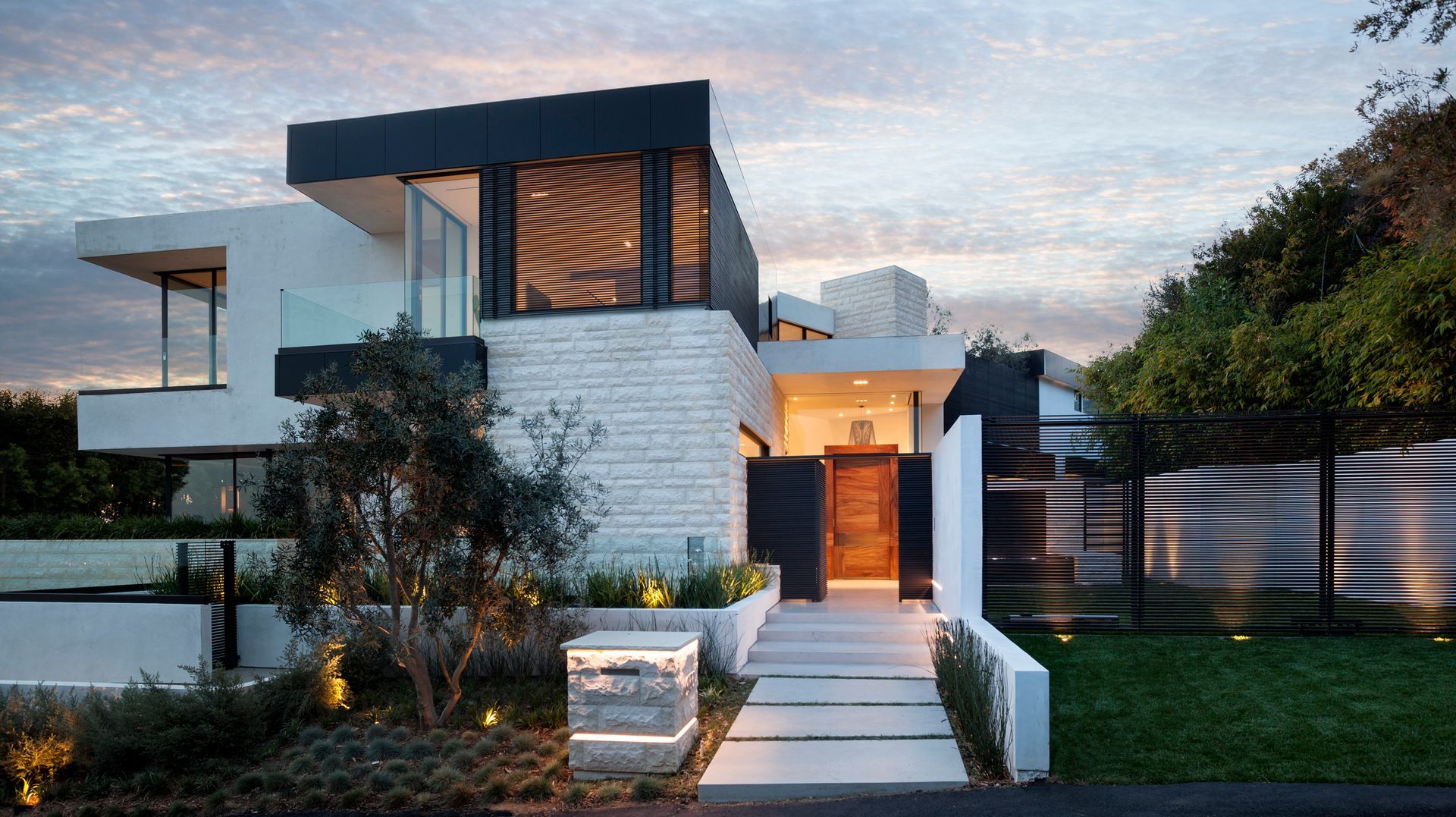 A modern house with a fence around it and trees in front of it