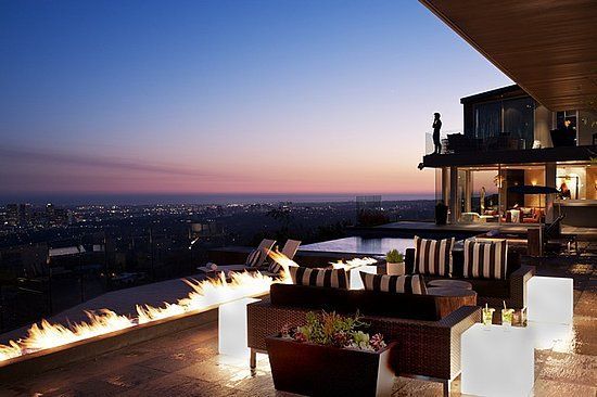 A patio with a fireplace and a view of the city at sunset.