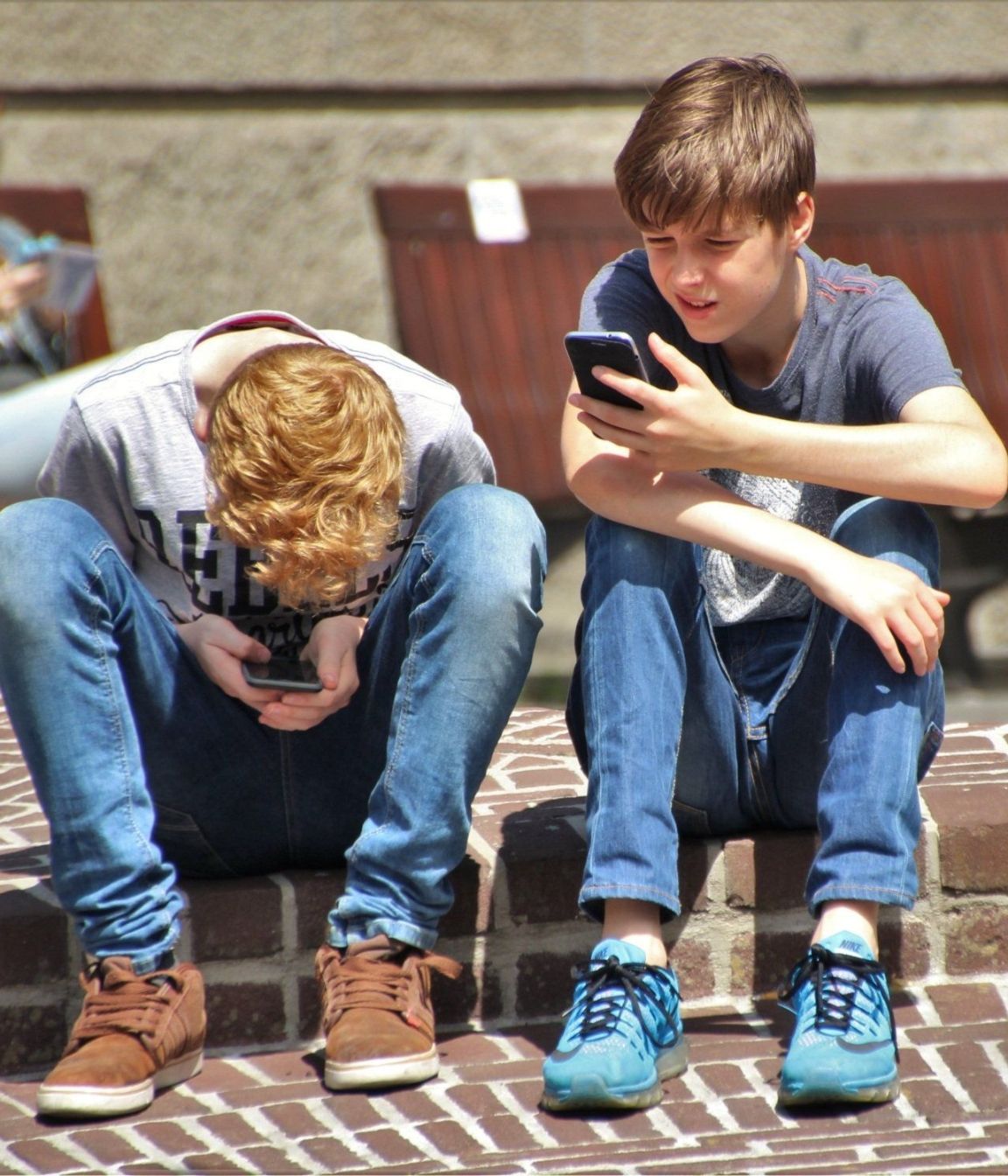 Teenagers Two boys are sitting on a brick sidewalk looking at their phones