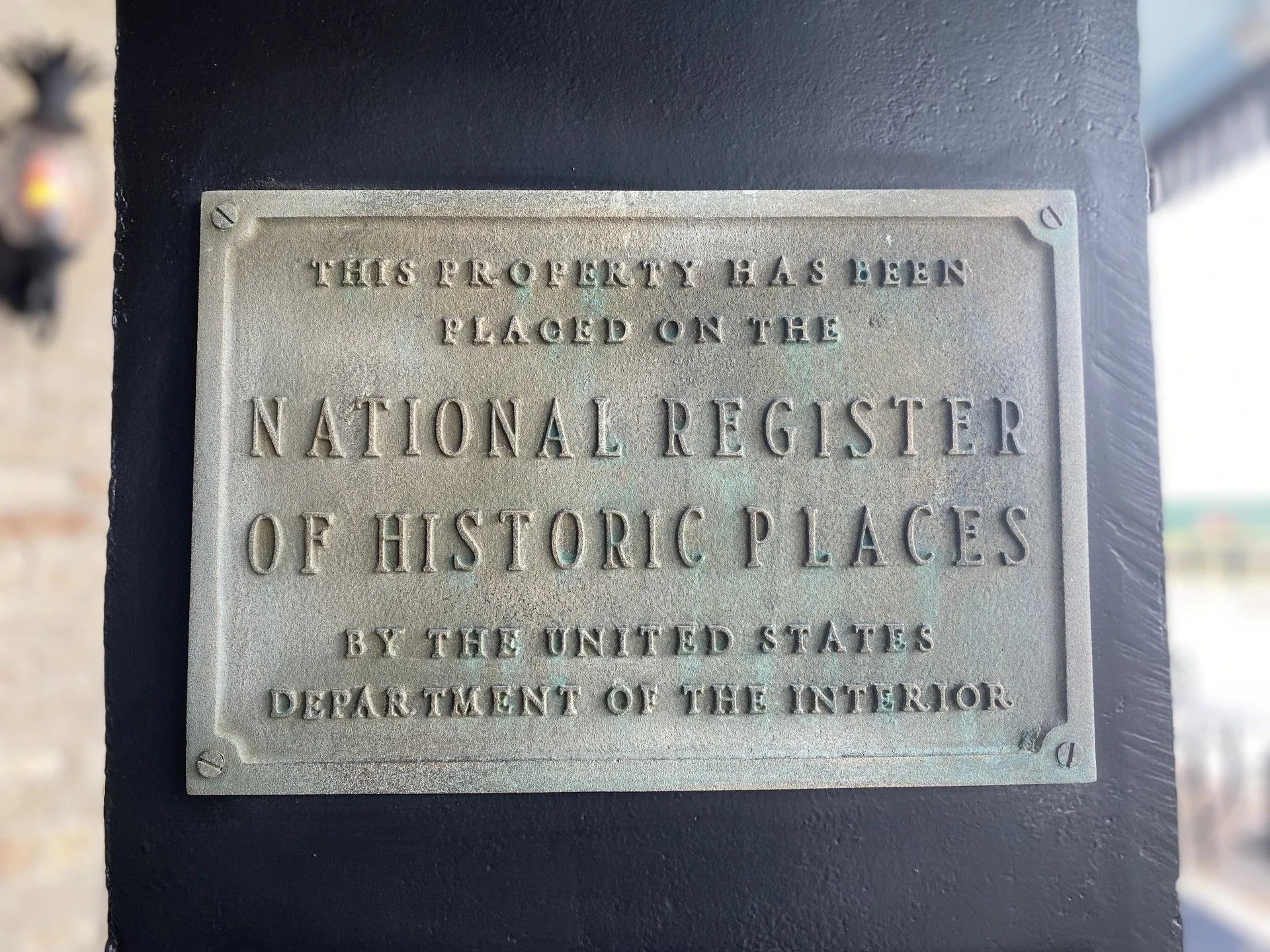 A bronze plaque on a dark post stating the property is on the National Register of Historic Places.