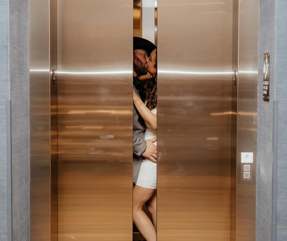 A couple shares a romantic kiss inside a partially closed, modern brass-toned elevator.