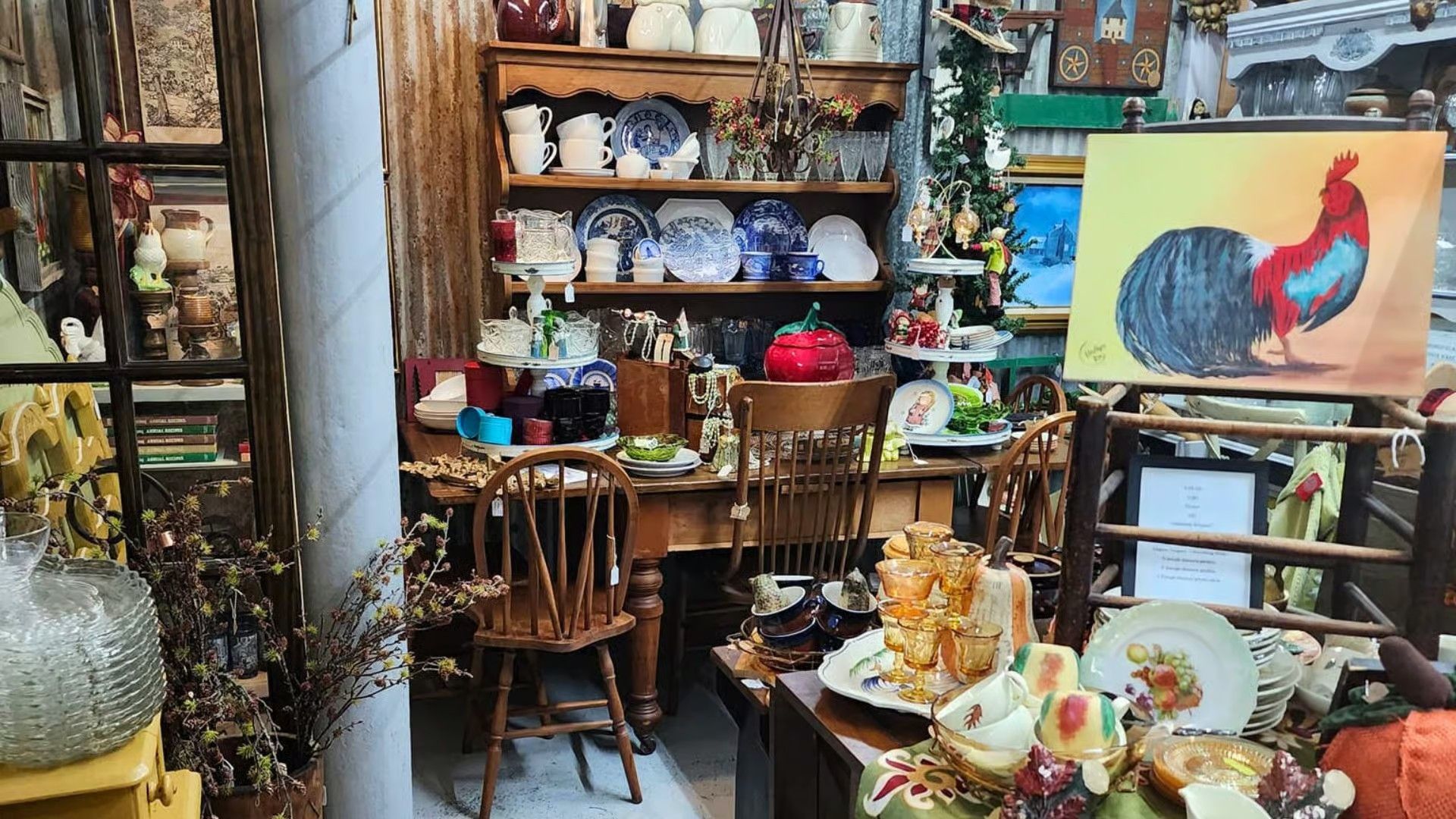 Antique shop interior with wooden furniture, a rooster painting, vintage china, and decor items on display.