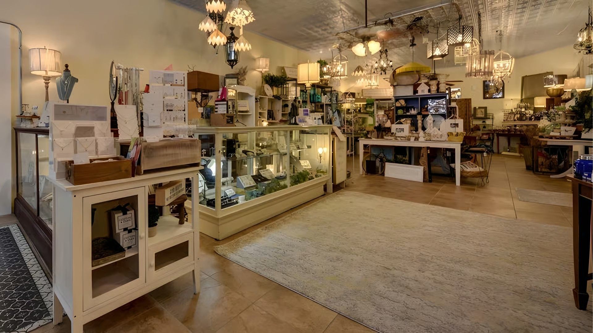 A brightly lit shop filled with antique lighting fixtures, glass display cases, and tables stocked with vintage goods.