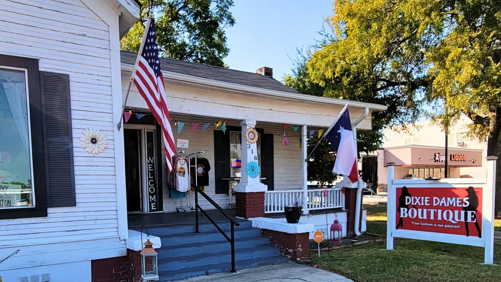 Dixie Darlin's Boutique shop housed in a white wooden building with a front porch, US and Texas flags, and a street sign.