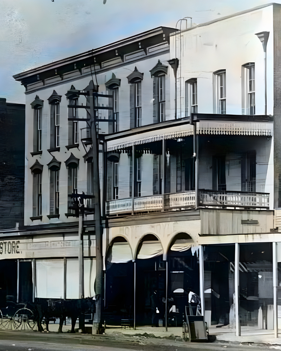 A vintage, three-story building with a distinctive second-floor balcony and arched lower columns beside a horse-drawn cart.