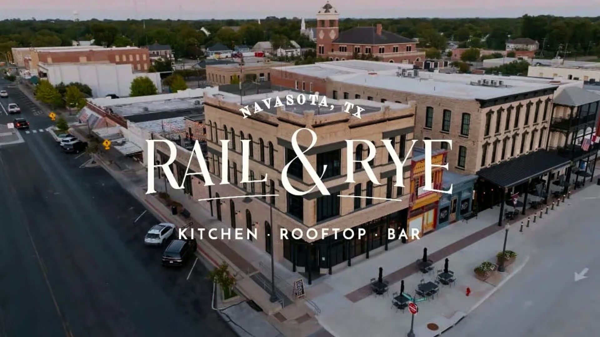 Aerial view of Rail & Rye restaurant in Navasota, Texas, located on a corner in a historic downtown area at dusk.