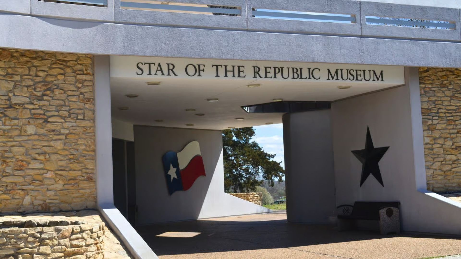 Entrance to the Star of the Republic Museum featuring a Texas flag and a large black star on the stone exterior walls.
