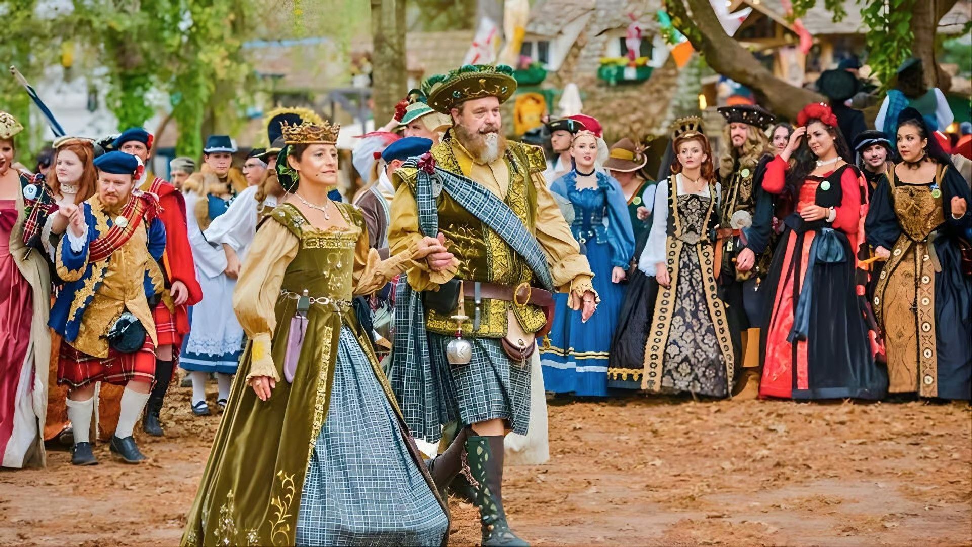 People in historical-style Renaissance costumes walk in a group on a dirt path at an outdoor festival.