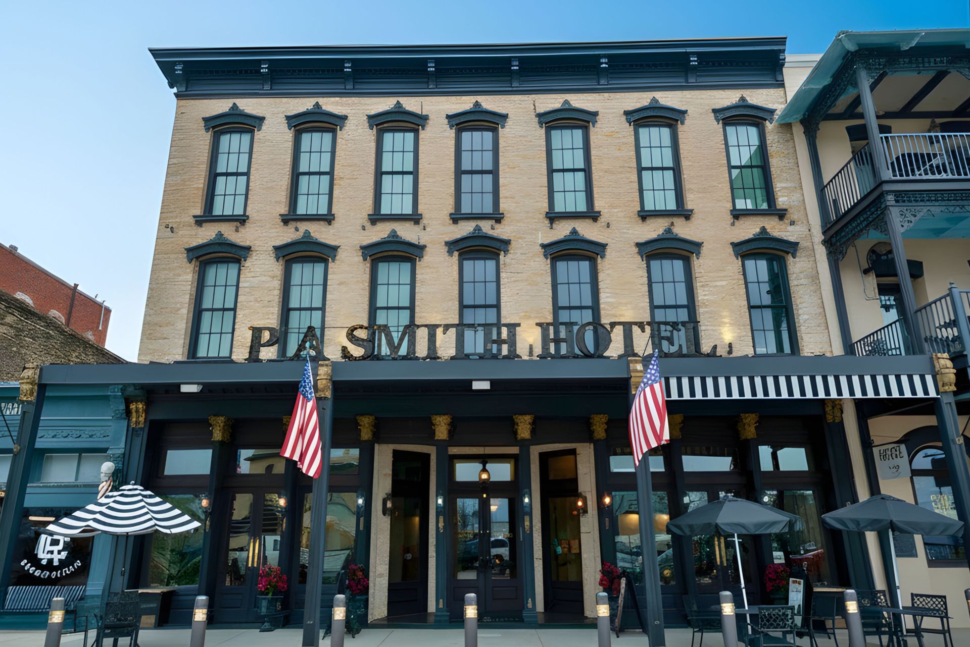 The three-story P.A. Smith Hotel building featuring tan stone, dark trim, and American flags at the entrance.