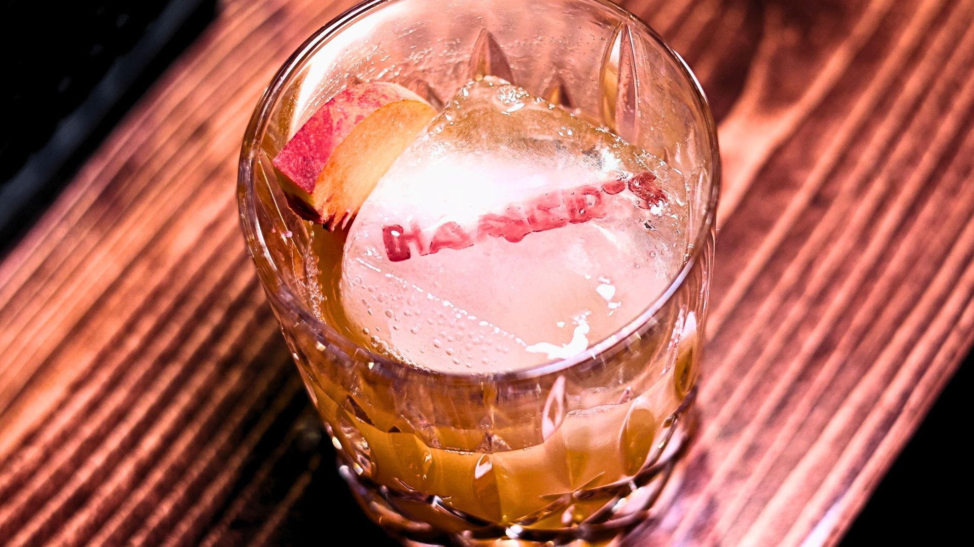 An interior view of a rustic, wood-paneled bar featuring a line of dark wooden stools, warm lighting, and a television.