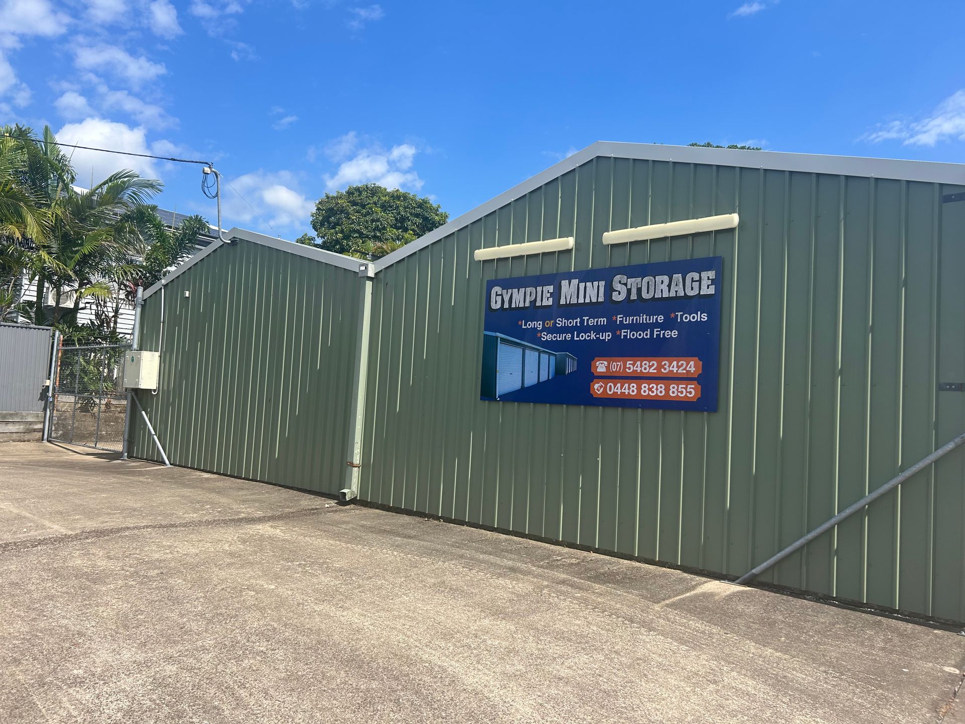 Green storage facility with sign: Olympic Way Storage. Blue sky, overcast day. — Gympie Mini Storage in Gympie, QLD