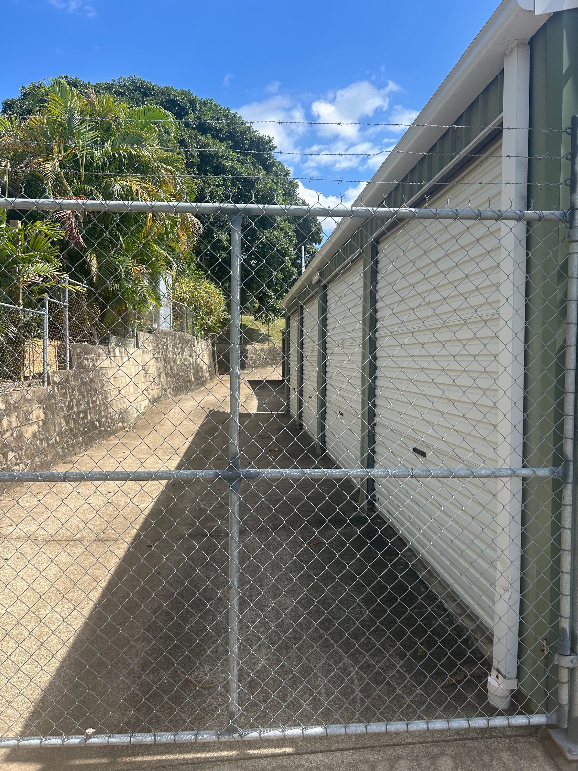 Chain-link fence in front of a row of white storage units, with a tree in the background. — Gympie Mini Storage in Gympie, QLD
