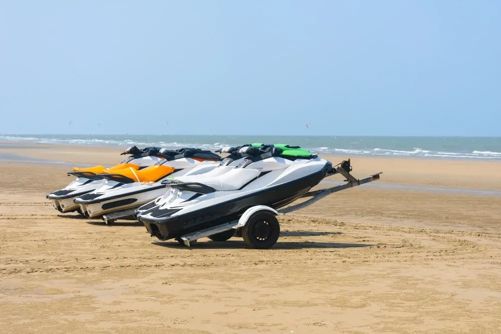 Three jet skis on a sandy beach under a blue sky. One is white and black, one orange, one green. — Gympie Mini Storage in Gympie, QLD