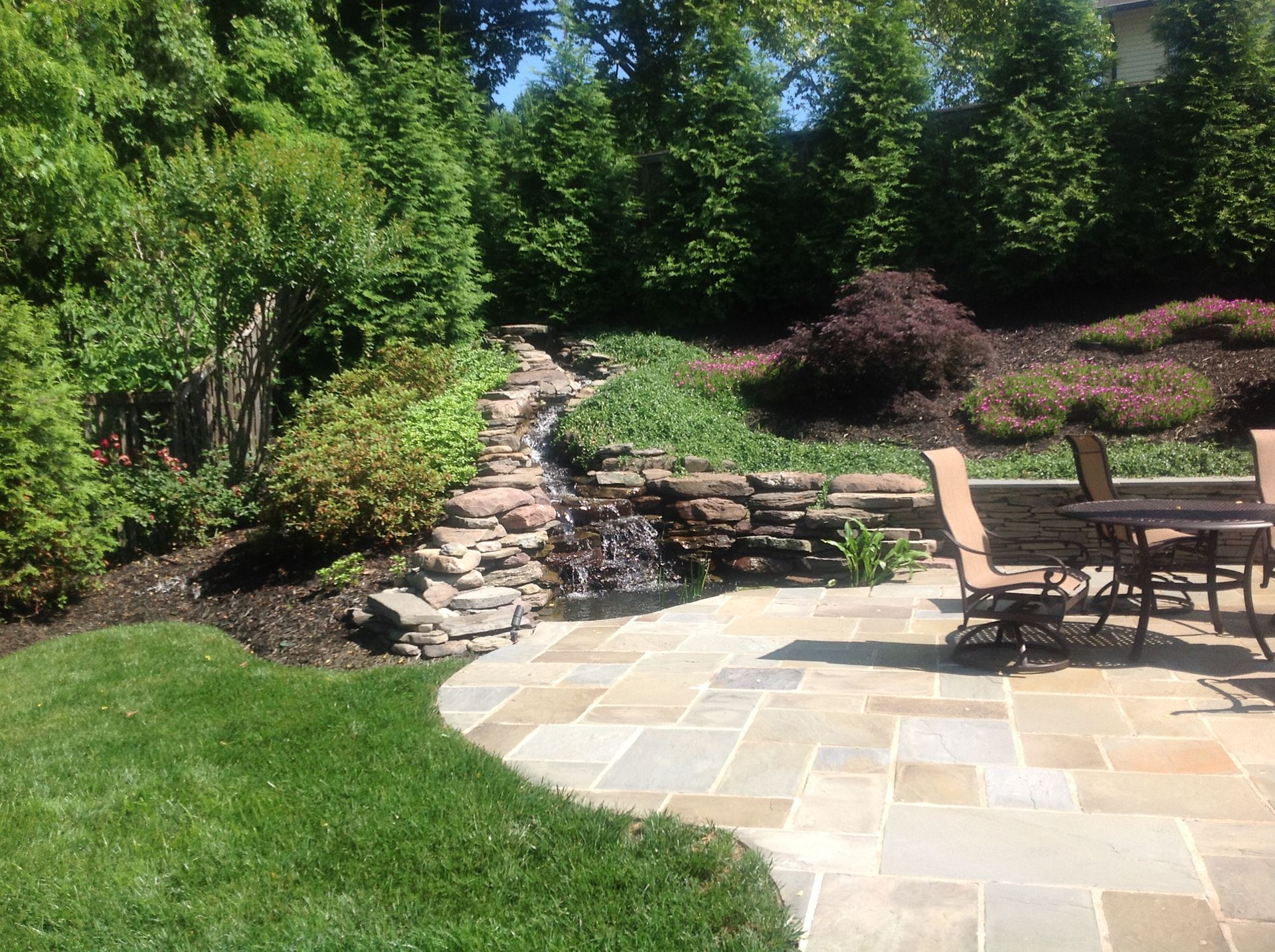 A patio with a table and chairs and a waterfall in the backyard.