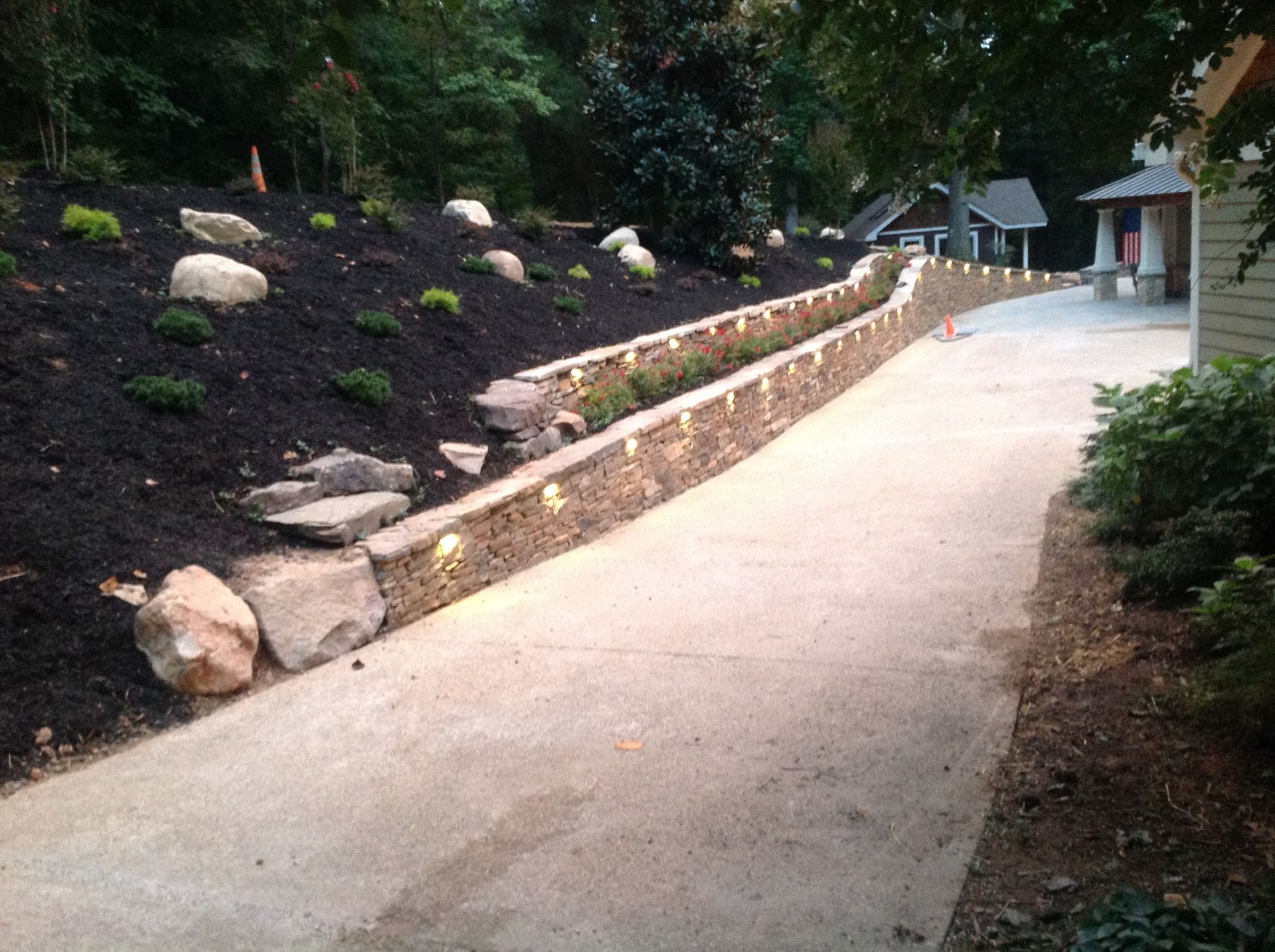 A driveway with a stone wall on the side of it and a house in the background.