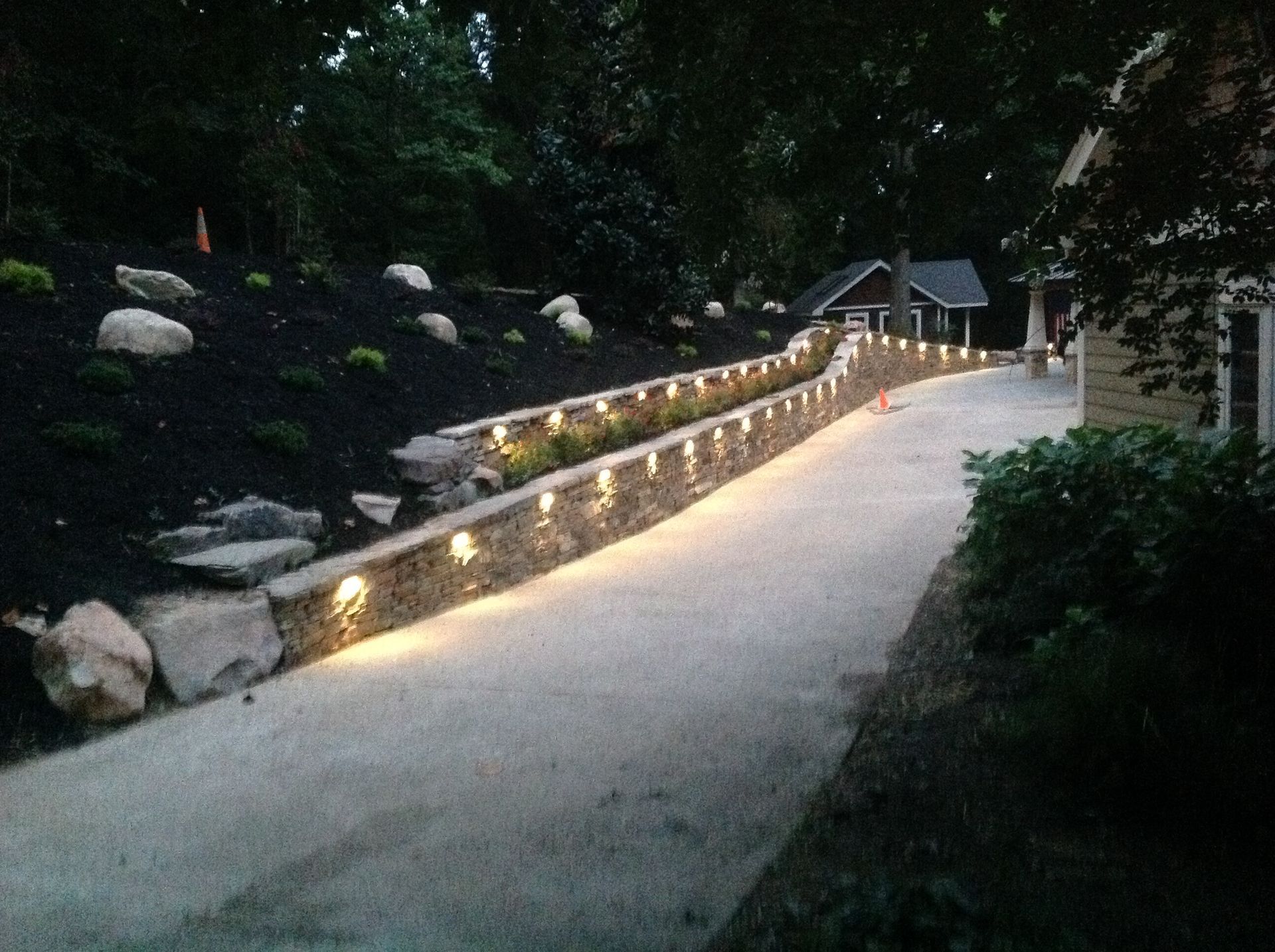 A driveway with a stone wall and lights on it