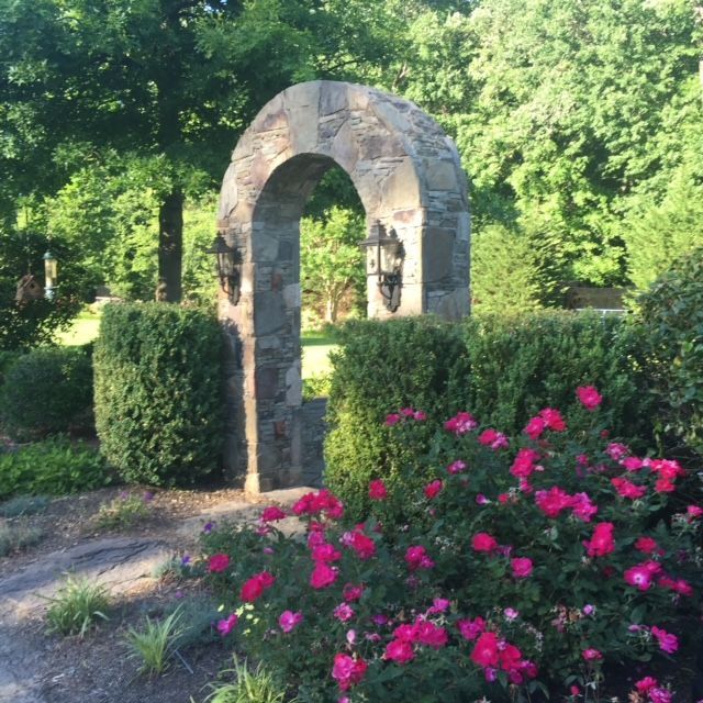A stone archway surrounded by bushes and pink flowers