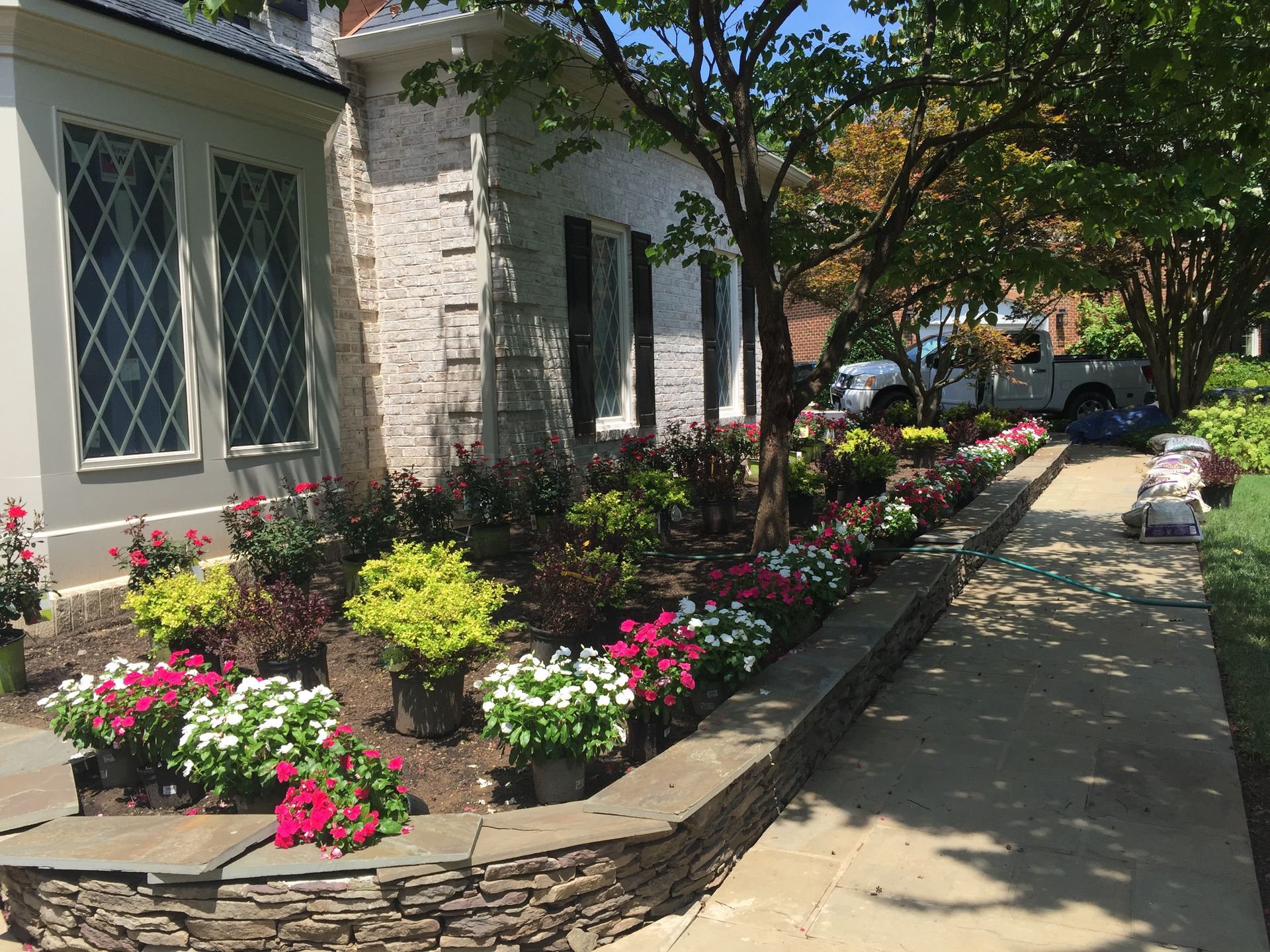 Landscspe design, a house front walkway and flower bed with a lot of flowers in front of it