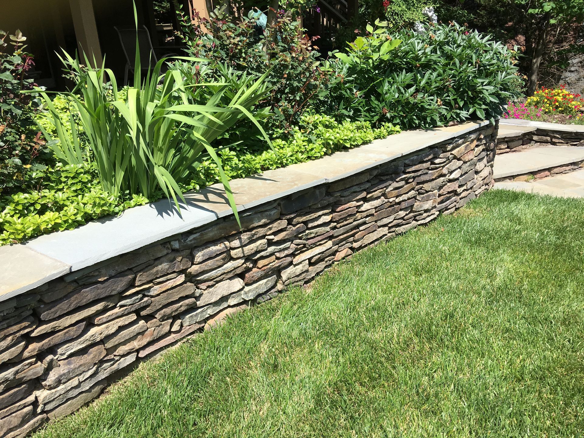 A stone wall surrounds a lush green lawn in a garden.