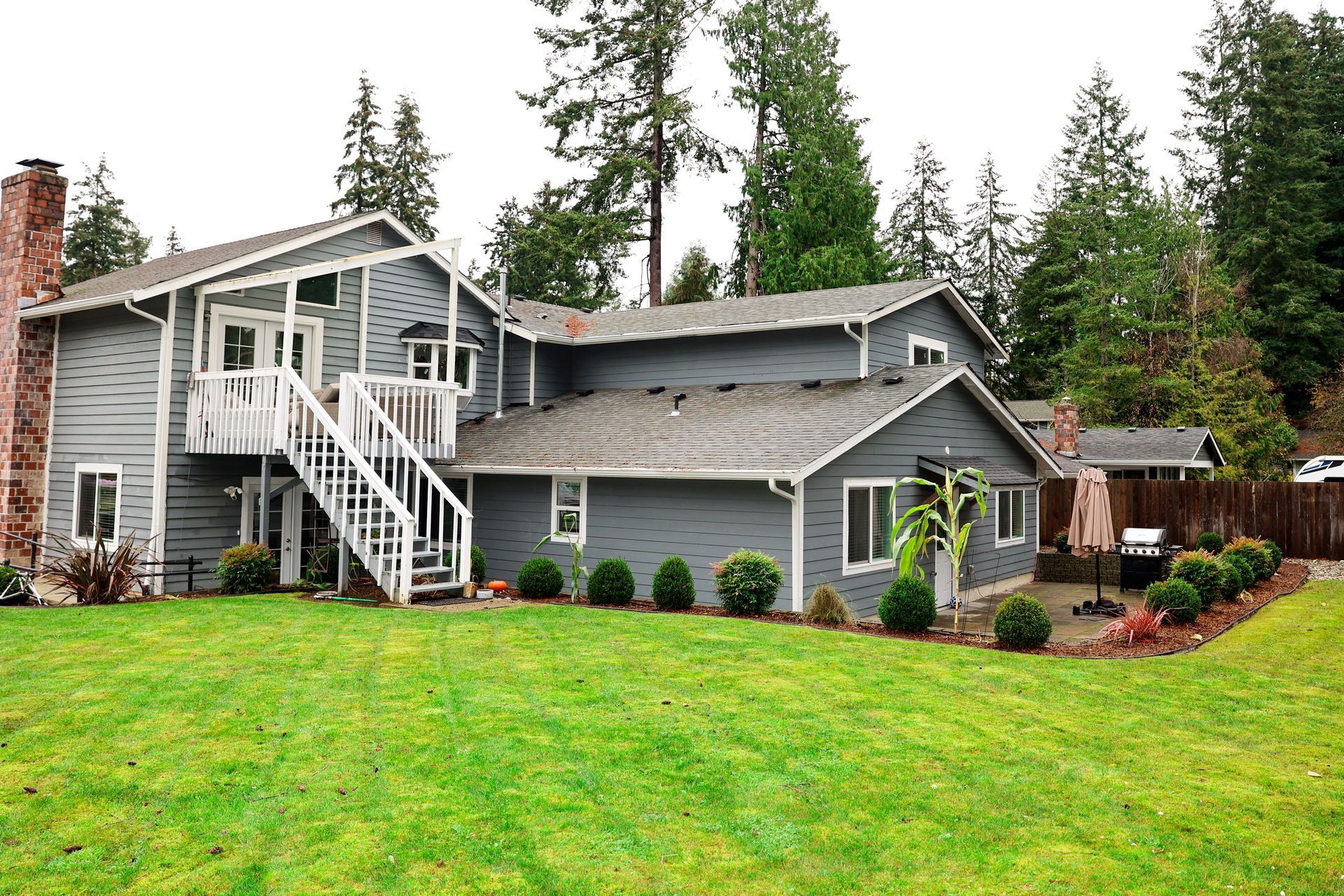A Grace of Love Adult Family Home Gray house with a chimney, white stairs, green lawn, and surrounding trees.