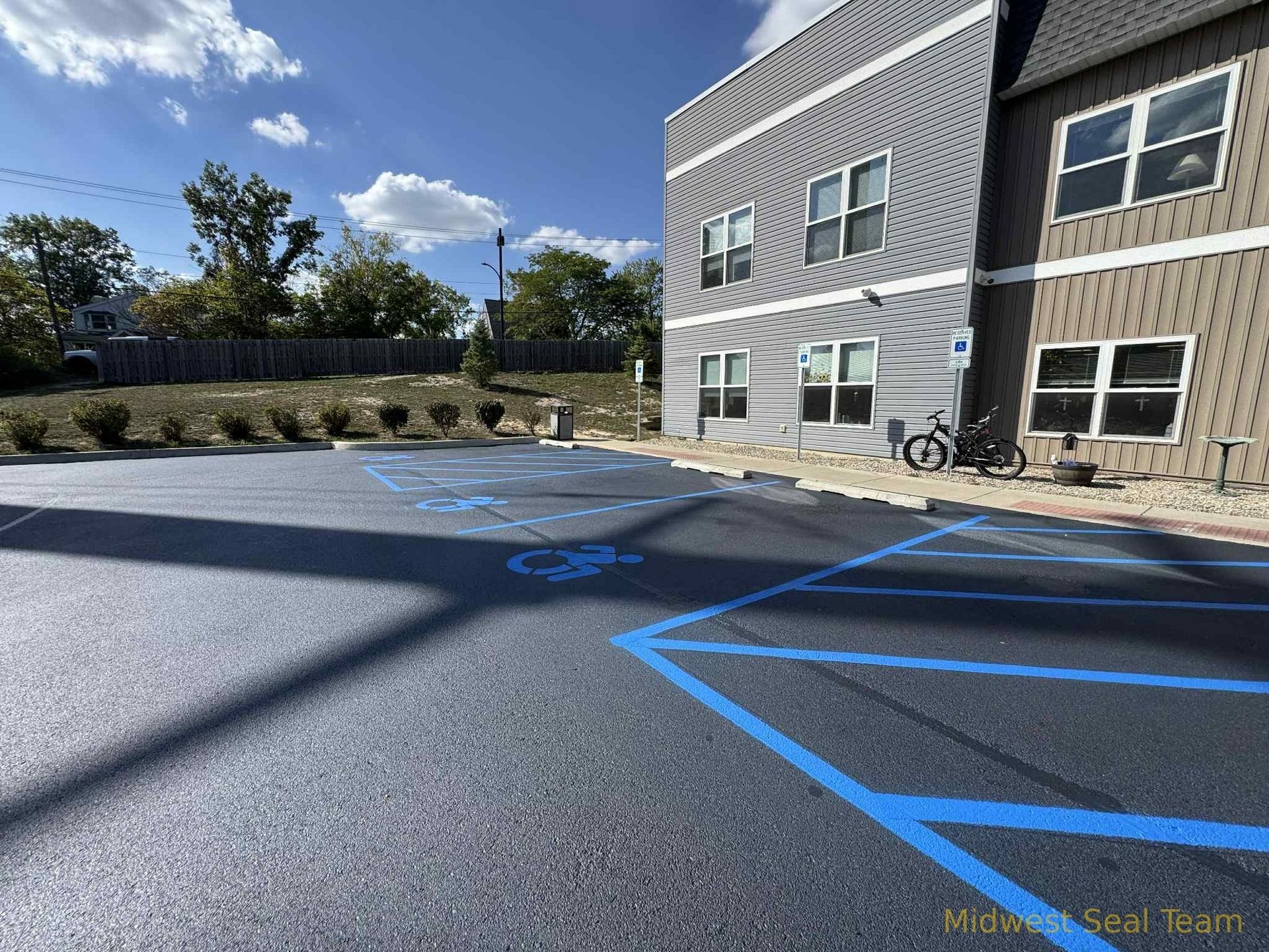 Image of Midwest Seal Team Sealcoating a parking lot in Auburn, IN. You can see the Midwest Seal Team crew working on sealcoating the edges of the parking area. 
