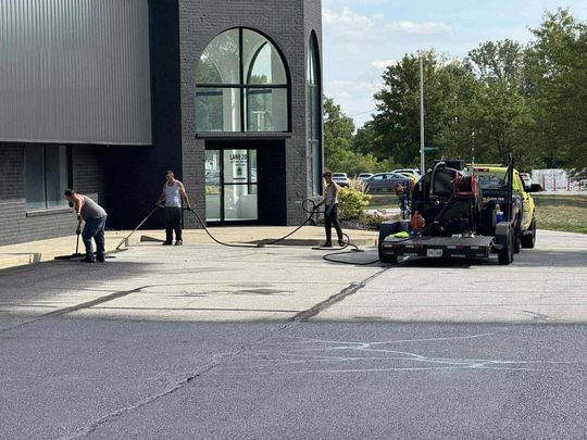 Image of Midwest Seal Team Sealcoating a parking lot in Fort Wayne, IN. You can see the Midwest Seal Team crew working on sealcoating the edges of the parking area. 