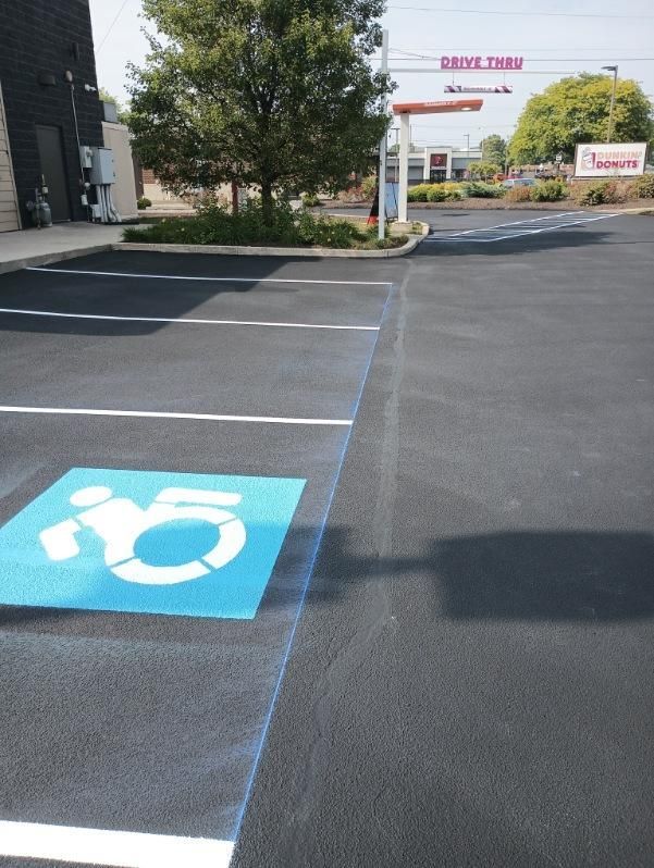 Image showing parking lot painting. You can see a blue handicap parking symbol and white parking lines. 