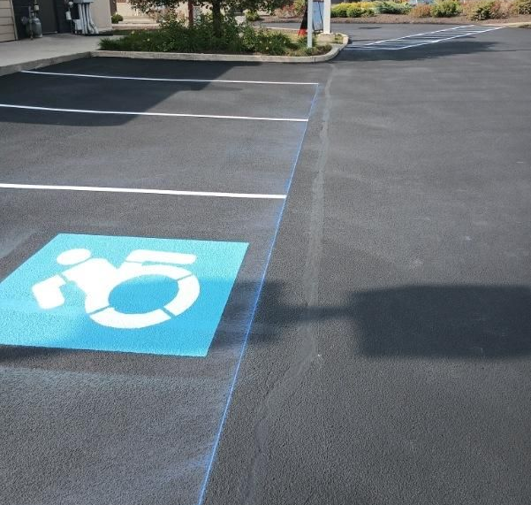 Image showing parking lot painting. You can see a blue handicap parking symbol and white parking lines. 