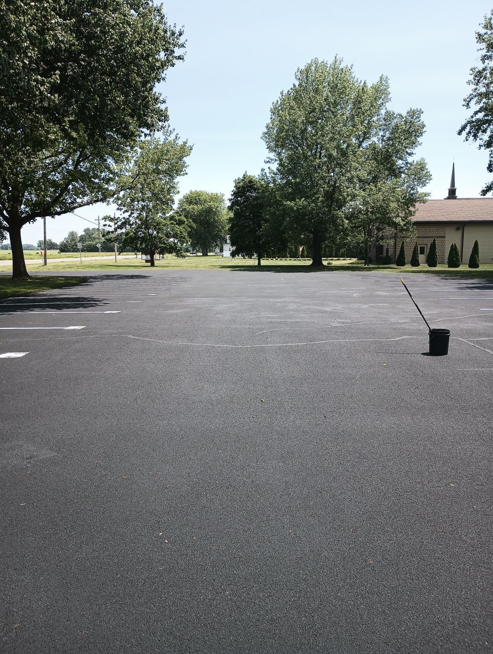 Image of a freshly sealcoated parking lot. You can see a newly sealcoated parking lot in Fort Wayne, IN, with a smooth, glossy surface reflecting the sunlight.

