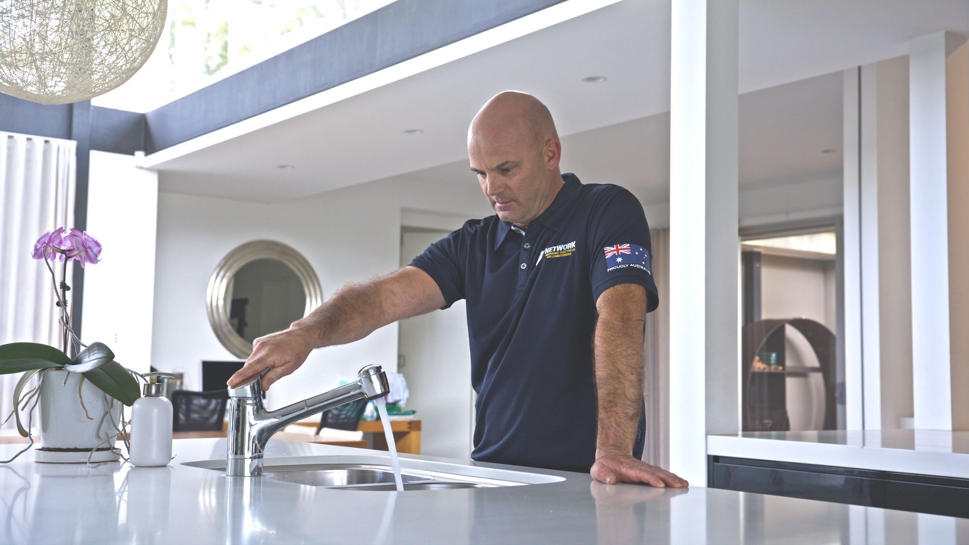 A plumber is fixing a tap in a kitchen.