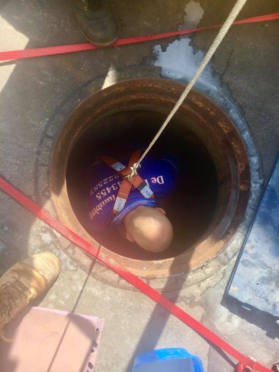 A Man is Hanging From a Rope in a Manhole — De Rose Plumbing In Bayview Heights, QLD
