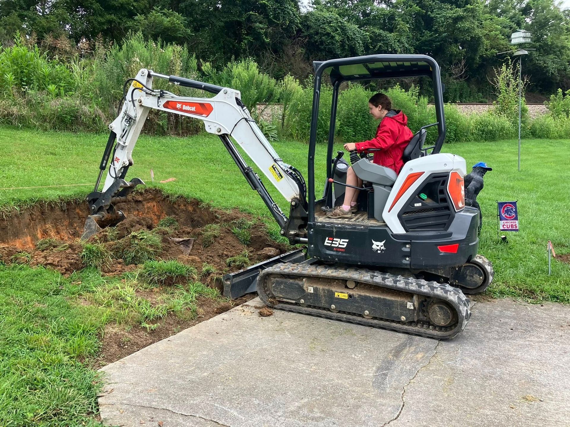 Yellow backhoe digging trench in asphalt road; dump truck nearby, dirt and debris visible.