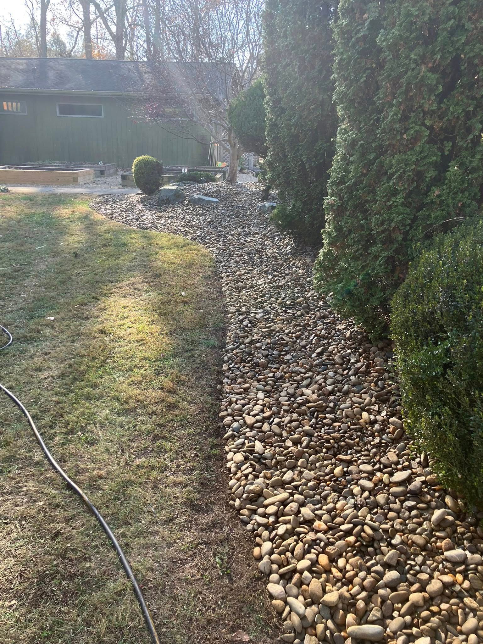 Man pushes a red lawnmower near a truck; two others stand in the background. Gravel and a cone are in the scene.