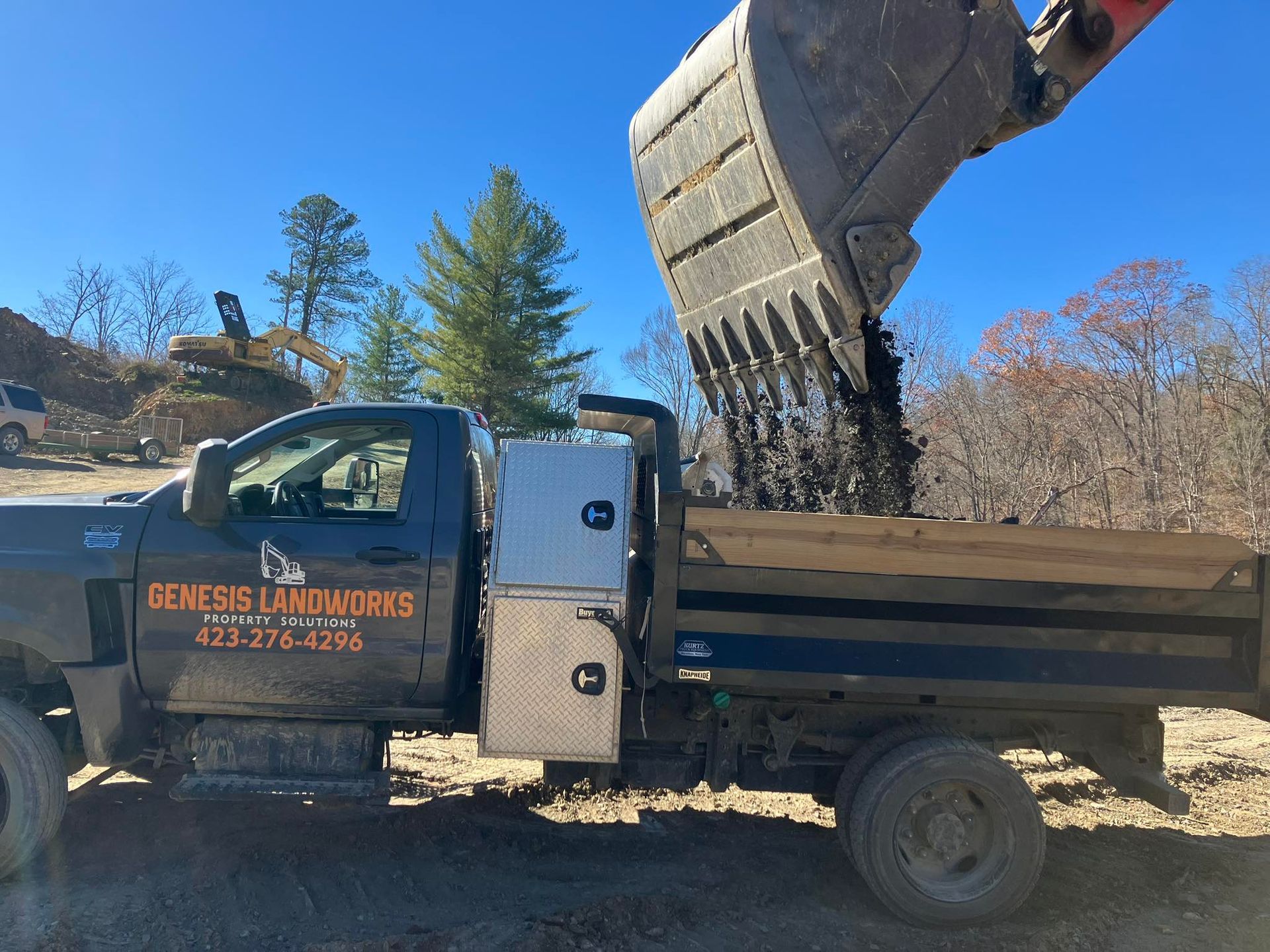 Yellow excavator on a mound of dirt at a construction site near brick buildings under a blue sky.