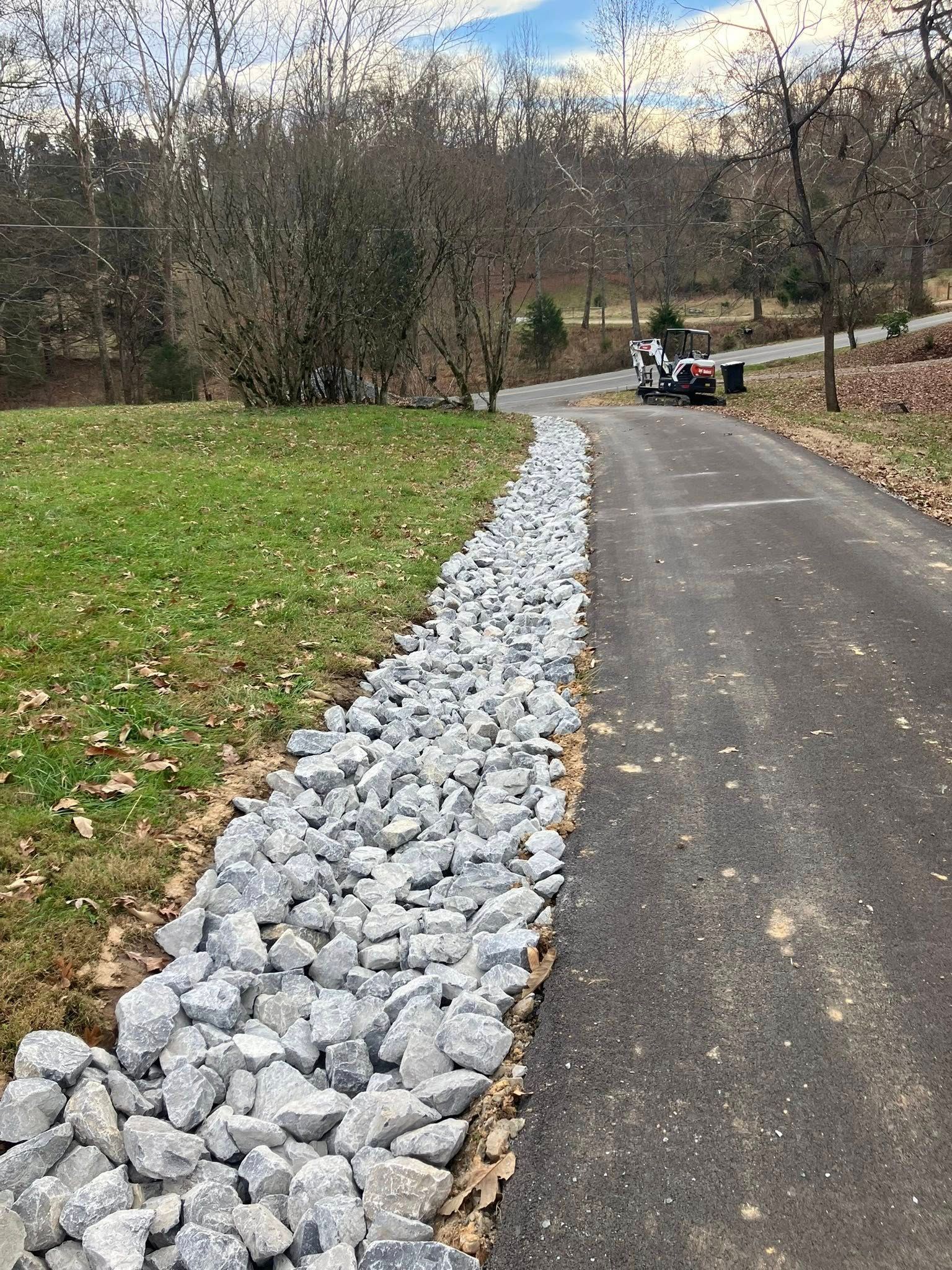 Yellow excavator digging into a dirt mound next to a fence in front of houses on a sunny day.