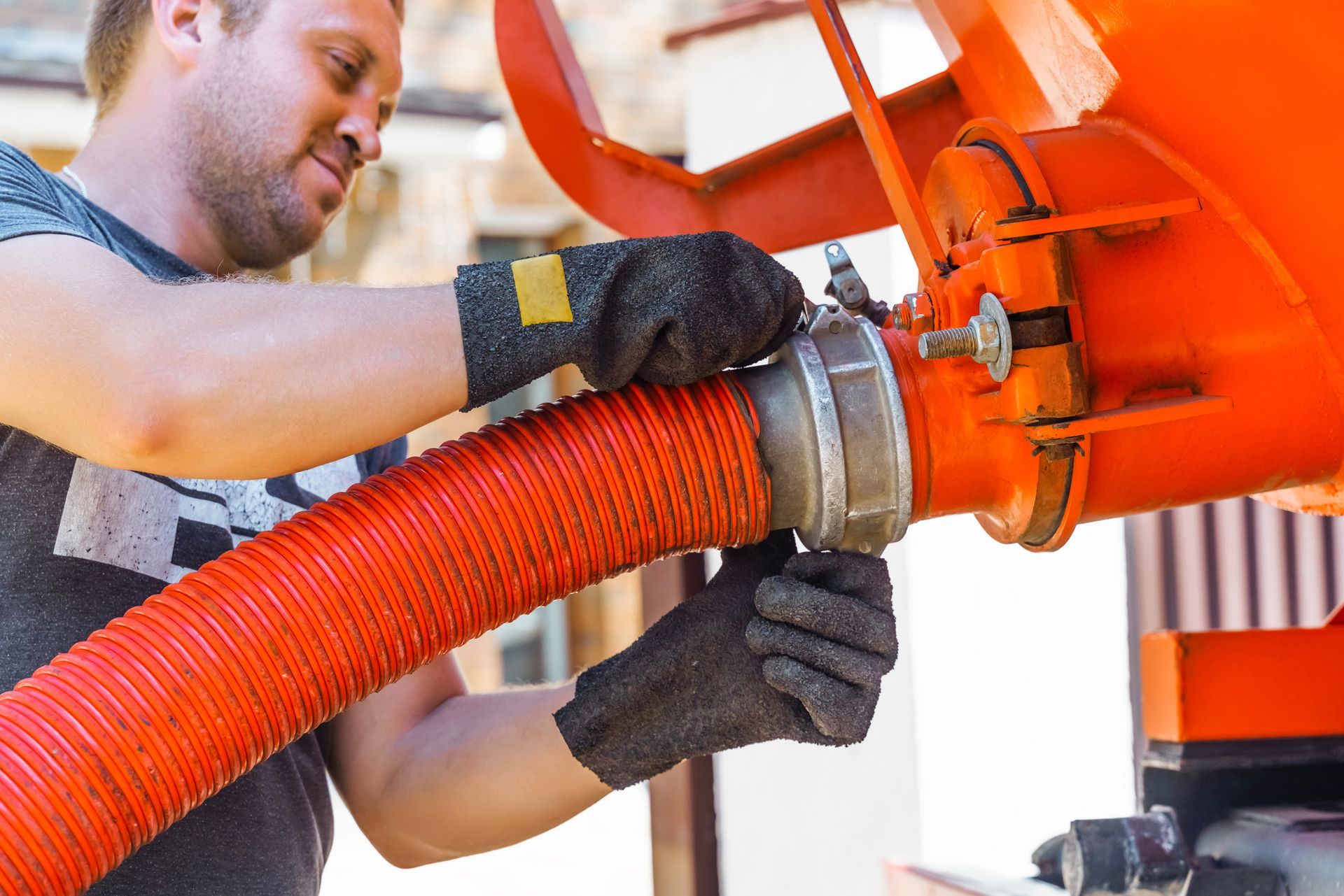 Man in gloves connecting a red hose to an orange tank.