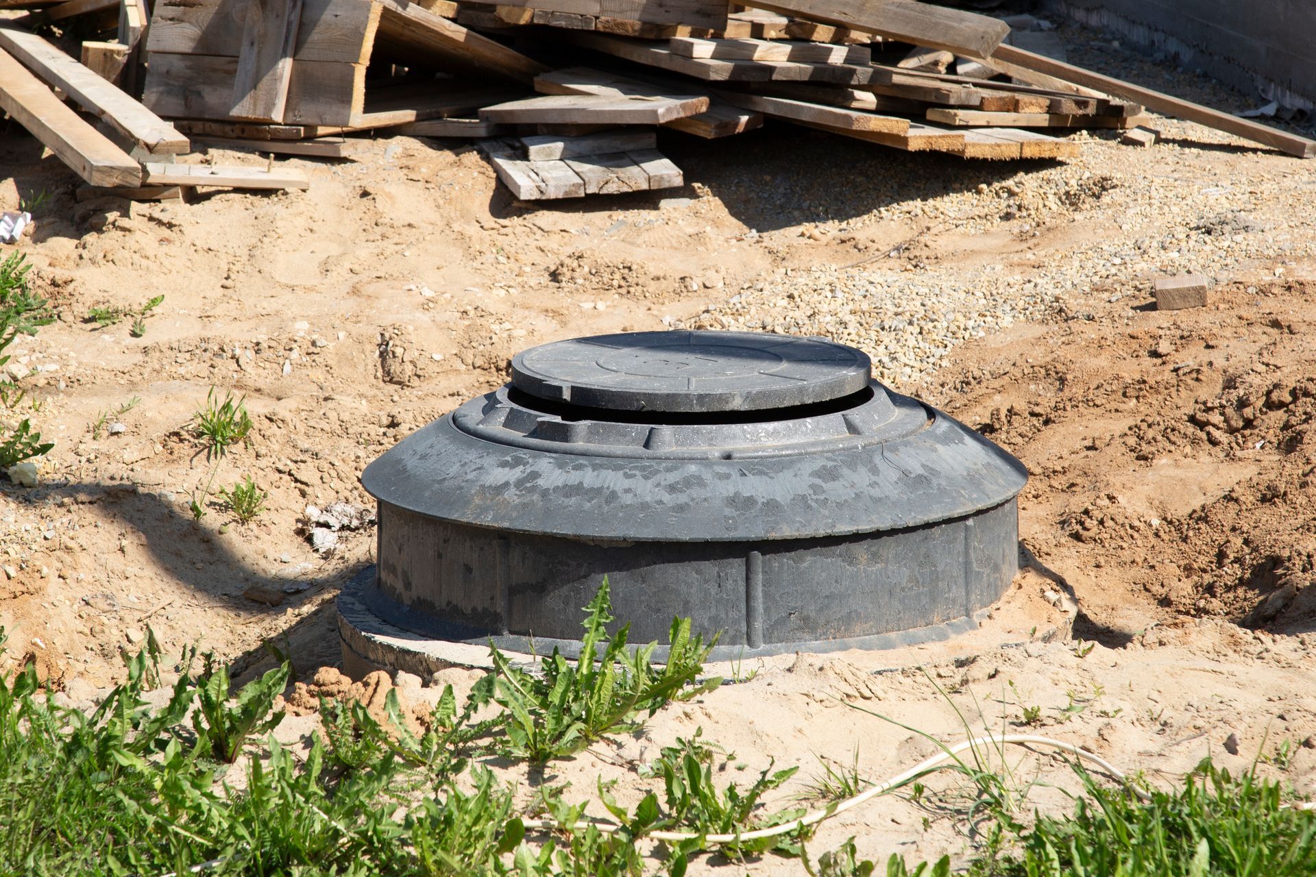 Concrete septic tank lid in sandy ground, with wood planks in the background.