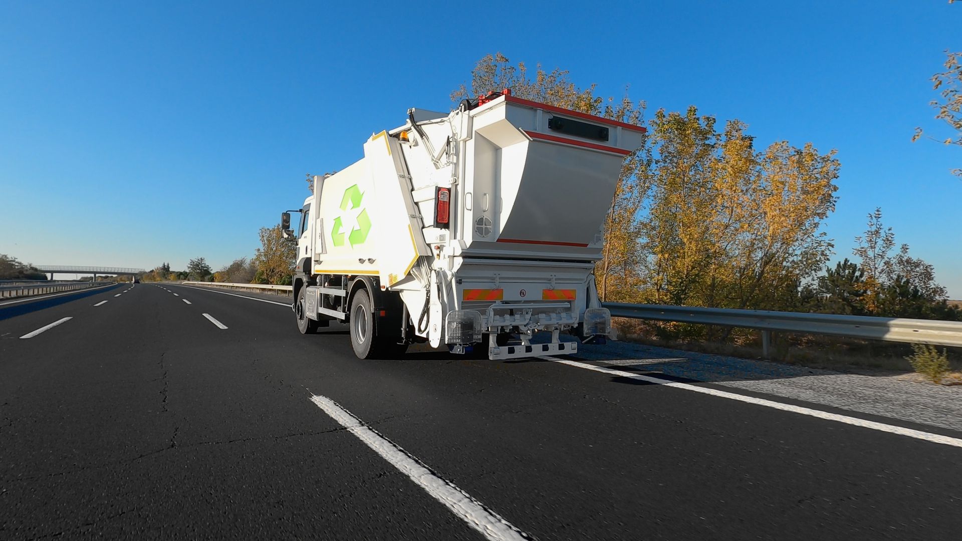 Garbage truck with recycling symbol driving on a highway on a sunny day.