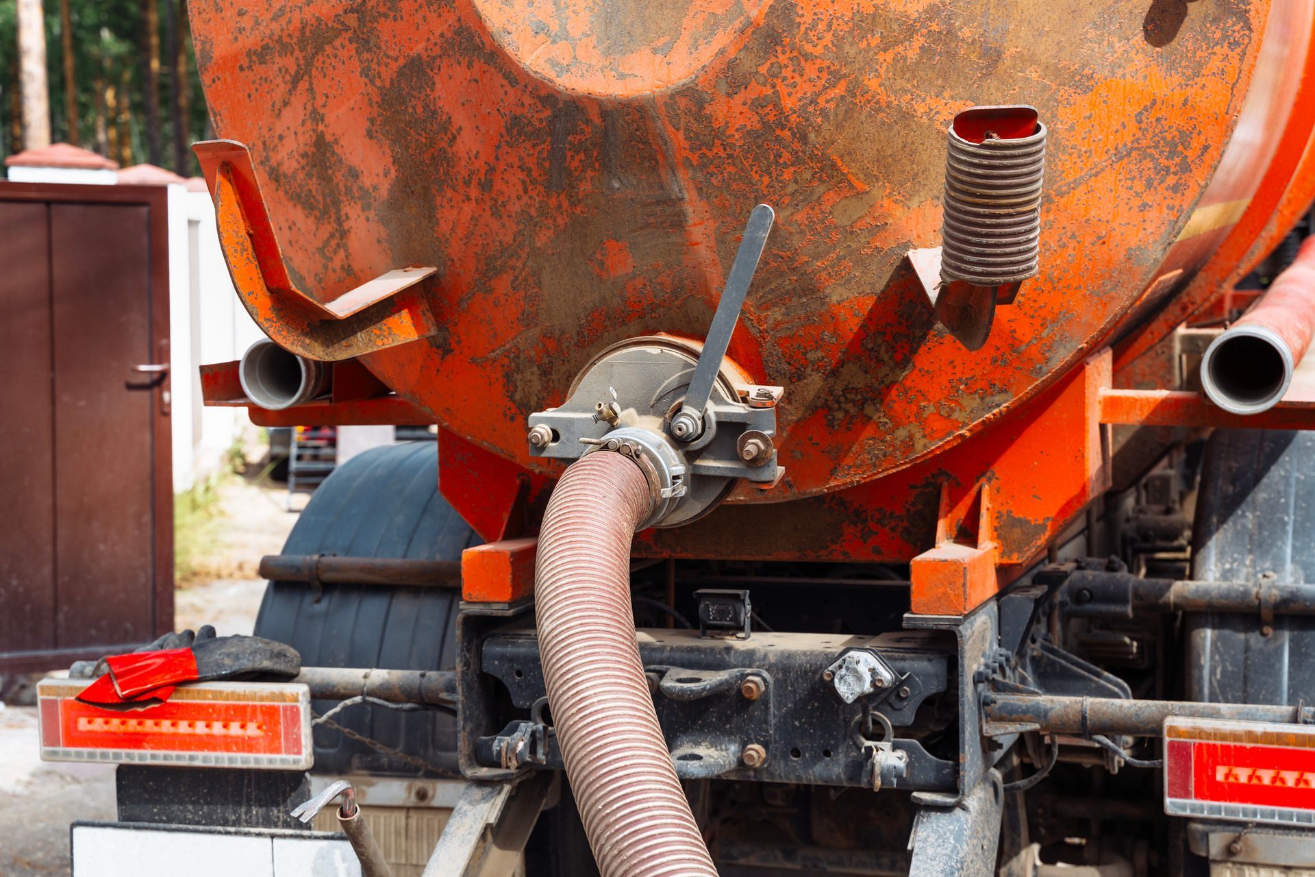 Back of an orange septic truck with a connected hose.