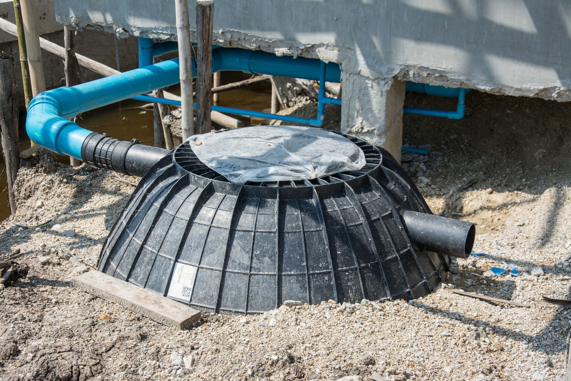 Black septic tank with a blue pipe, installed outdoors.