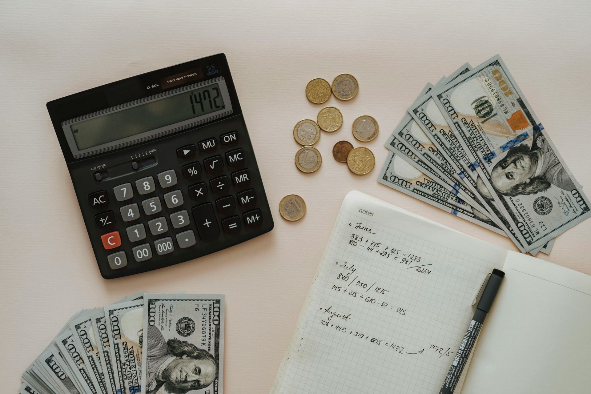 A calculator , money , coins and a notebook with a pen on a table.