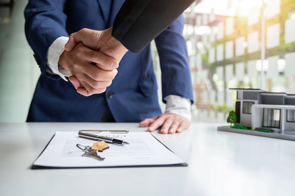 A man in a suit is shaking hands with a woman in front of a model house.