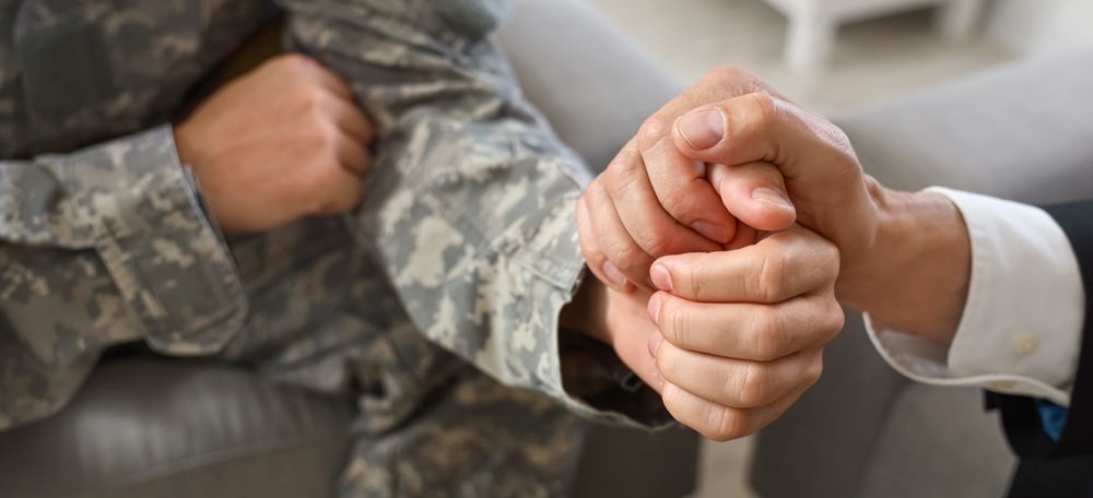 A man in a suit is holding the hand of a soldier in a military uniform.