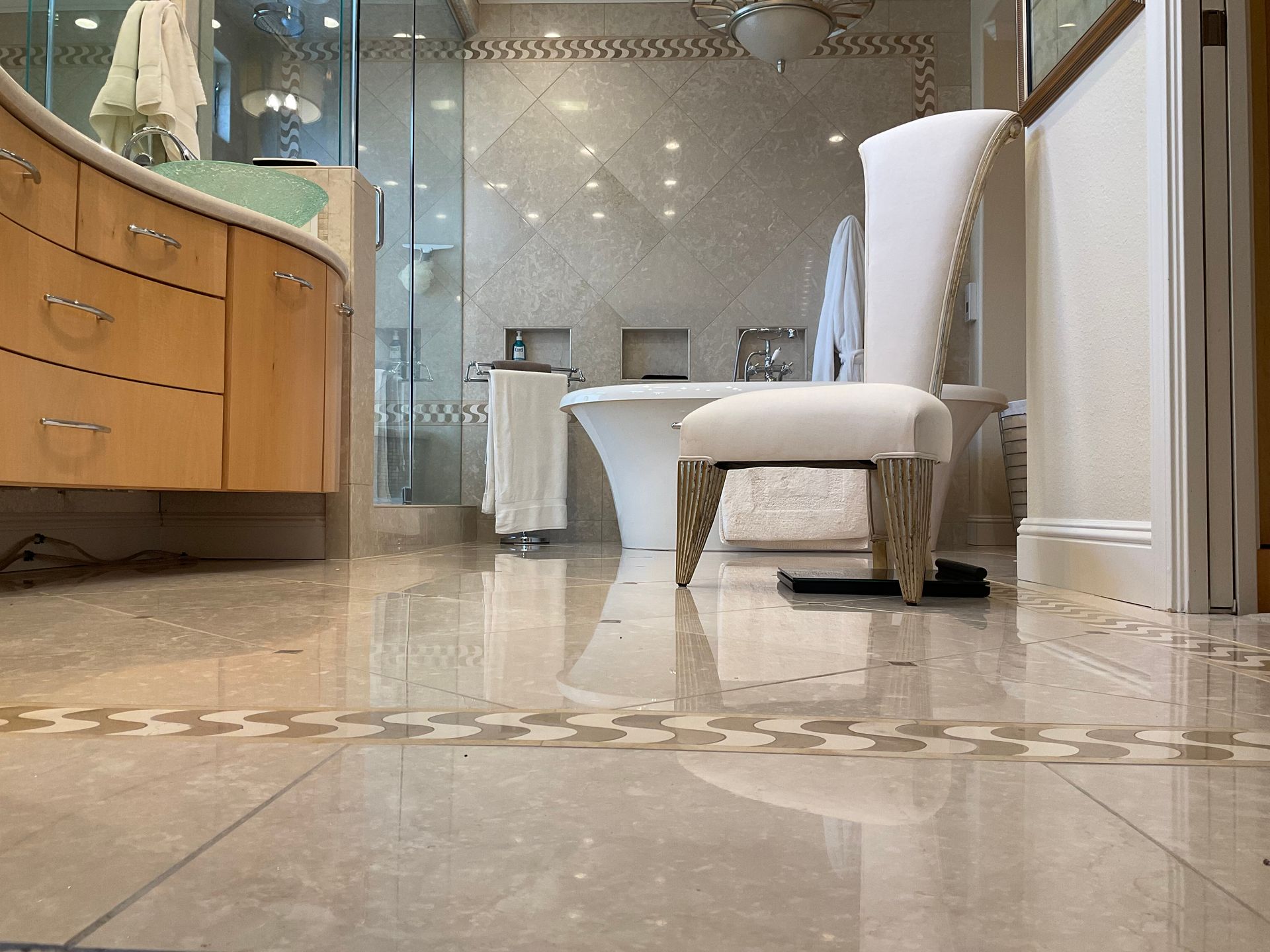 Bathroom with a white chair in the center. Light wood cabinets, a bathtub, and tiled floor are visible.