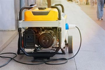 Yellow and gray portable generator on a sidewalk, powering a nearby device.