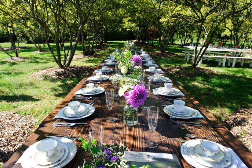 A long wooden table with plates , cups , glasses and flowers on it.